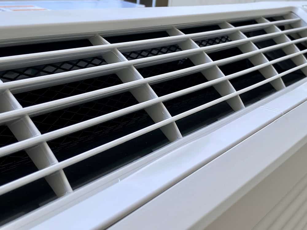 Close-up view of white air conditioner vents, showing the horizontal slats and dark grille behind them.